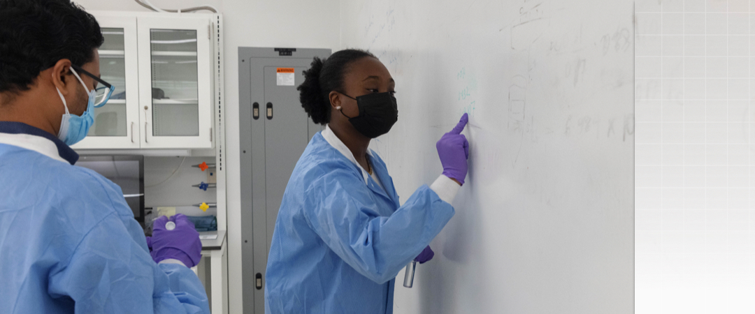 students in lab safety gear writing on whiteboard